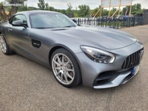 Mercedes-AMG GT Coupé gris mat, vue 3/4 avant, jantes argentées. Détail V8 BITURBO sur l'aile latérale. Garée sur asphalte.