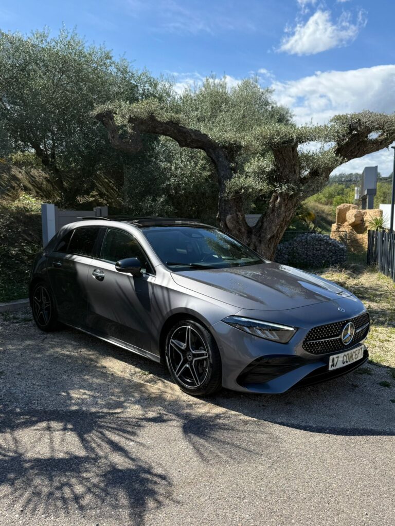Mercedes Classe A Grise : Élégance Moderne Sous l'Olivier Mercedes-Benz Classe A grise garée sous un vieil olivier, avec toit ouvrant panoramique et jantes noires. Plaque A7 CONCEPT.