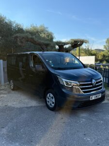 Van Renault Trafic gris foncé garé sur un parking, devant de vieux oliviers et un ciel bleu. Plaque A7 CONCEPT visible.
