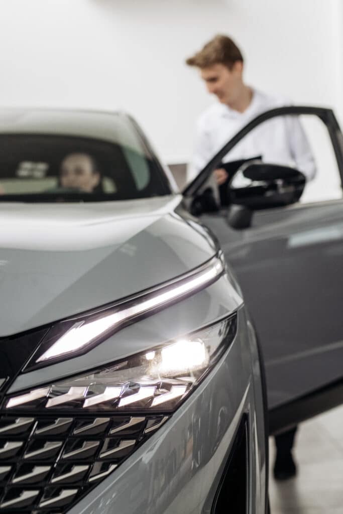 SUV gris avec phares LED allumés dans un concessionnaire. Un vendeur interagit avec un client près de la portière ouverte.