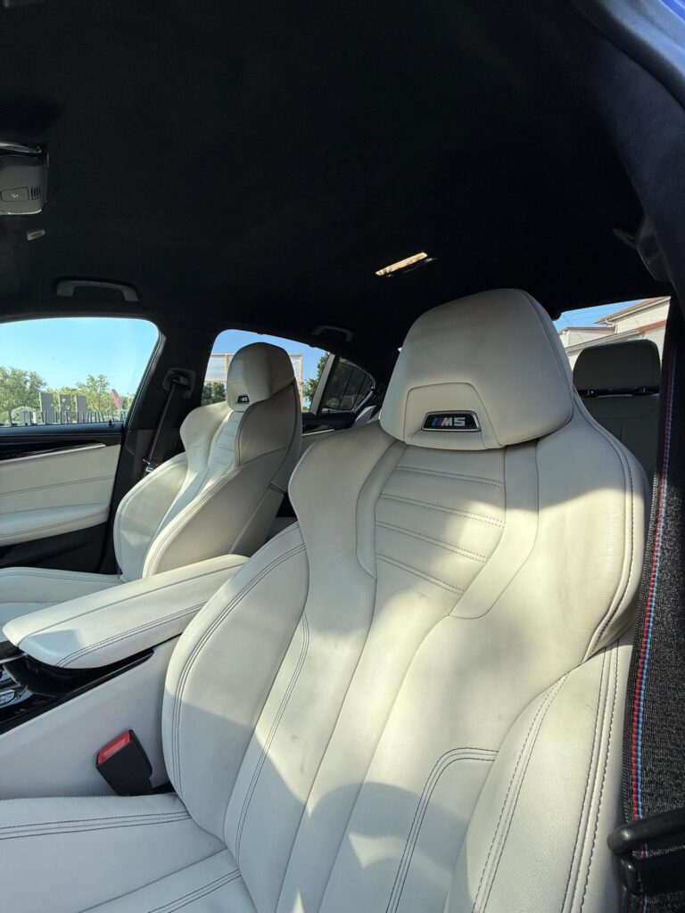 Intérieur cuir blanc de BMW M5 avec ciel de pavillon noir et logo M5 brodé sur les appuie-têtes.