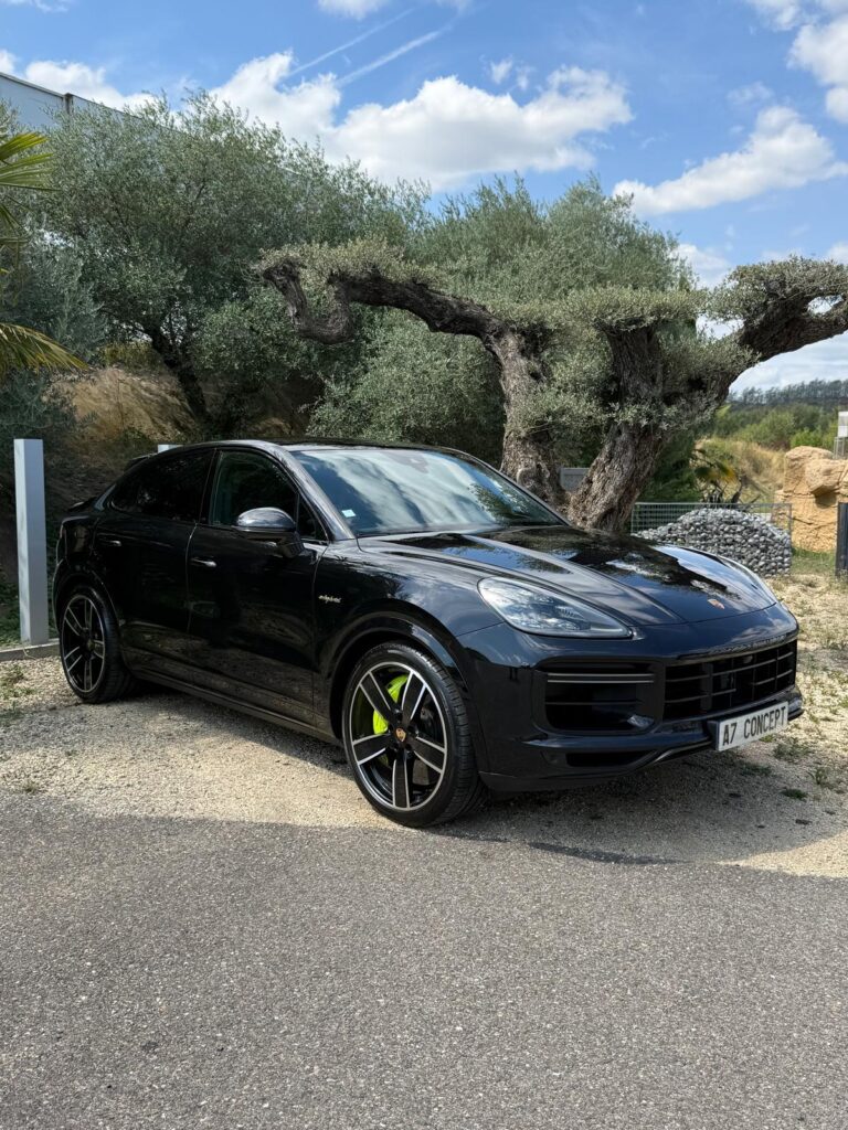 Porsche Cayenne Coupé hybride noir avec étriers de frein verts vifs, garé devant de vieux oliviers sous un ciel bleu. Plaque A7 CONCEPT.