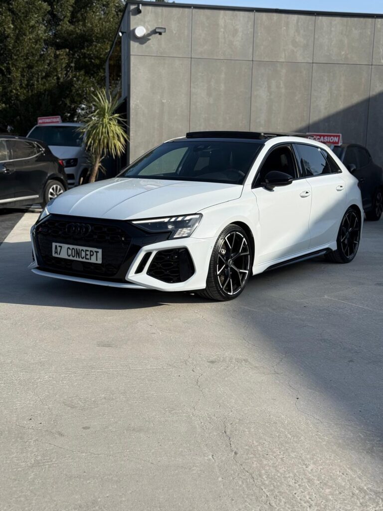 Audi RS3 Sportback blanche, plaque A7 CONCEPT, jantes alliage noires et toit panoramique sur parking extérieur.